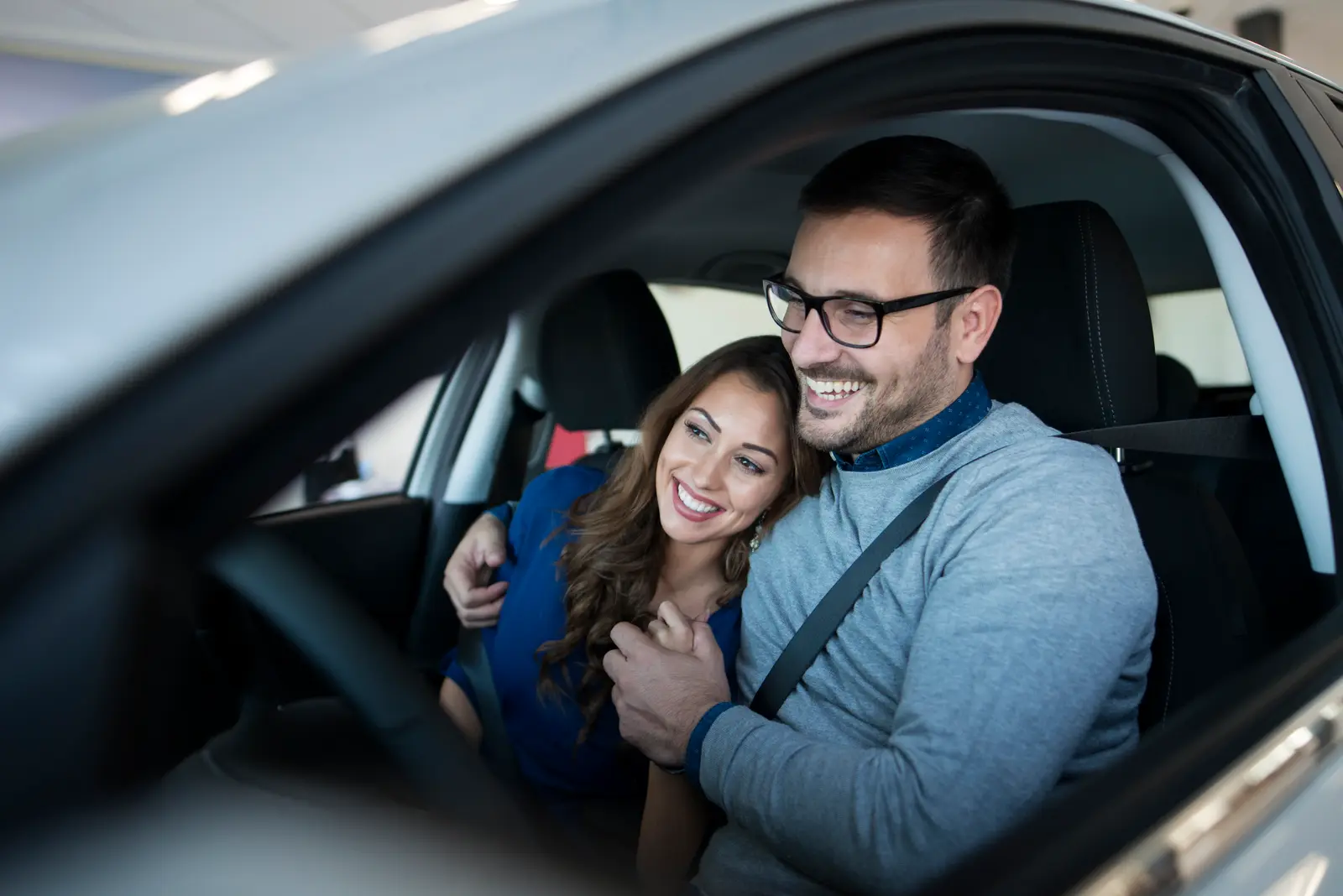 Pareja sonriendo dentro de su auto nuevo